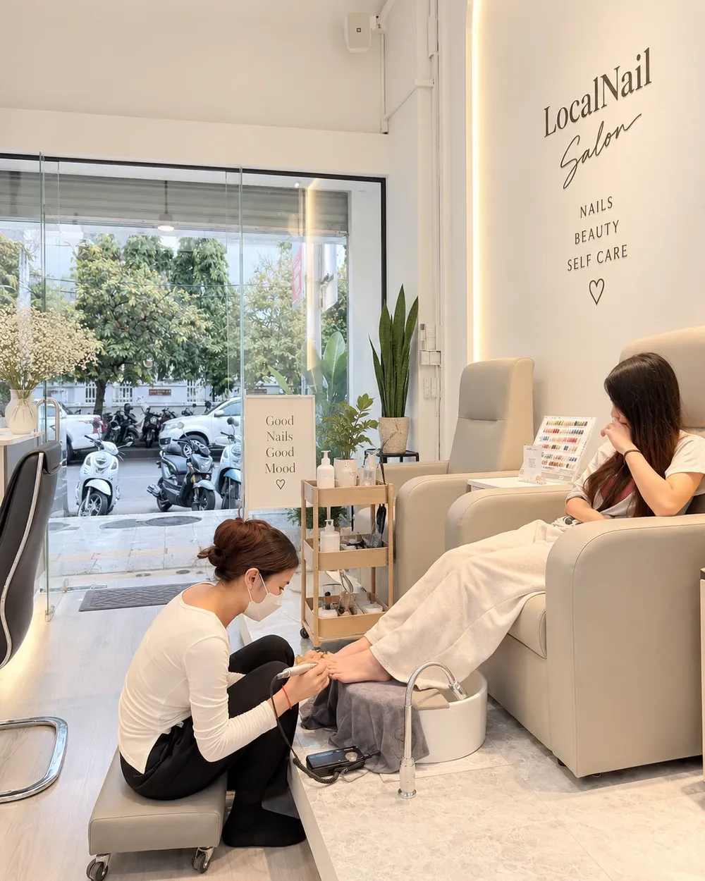 Inside LocalNail Salon: a client relaxing in the pedicure chair while a technician works, below the LocalNail Salon wall sign